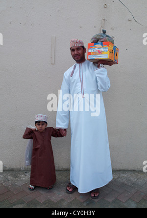 Padre e Figlio entrambi indossando il tradizionale Dishdasha e trasporto merci, IBRA, Oman Foto Stock