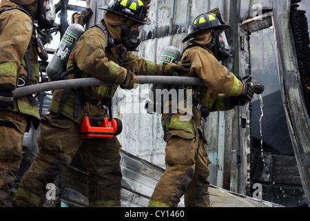 La donna pompiere su una linea flessibile di estinguere un incendio in un edificio industriale Foto Stock