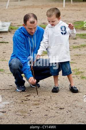 Un padre aiuta il suo autistico di cinque-anno-vecchio figlio di scrivere il suo nome nel fango. Foto Stock