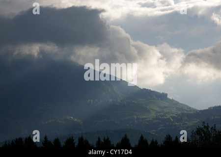 Un albero di luce irrompe attraverso le nubi e illumina le verdi pendici delle Alpi Kamnik, Gorenjska, Slovenia. Foto Stock