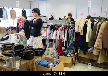 Le donne di rack di esplorazione di seconda mano vestiti e merci in vendita in un negozio di carità parsimonia store accozzaglia vendita regno unito Foto Stock