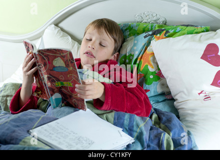 Giovane ragazzo caucasico iIn letto con influenza facendo lavori scolastici Foto Stock