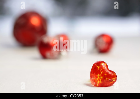 Piccolo rosso cuore di vetro con rosso baubles di Natale sulle bianche tovaglie Foto Stock