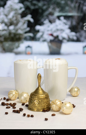 Golden Christmas bell e tazze da caffè, palle di Natale e i chicchi di caffè nella parte anteriore della terrazza invernale Foto Stock