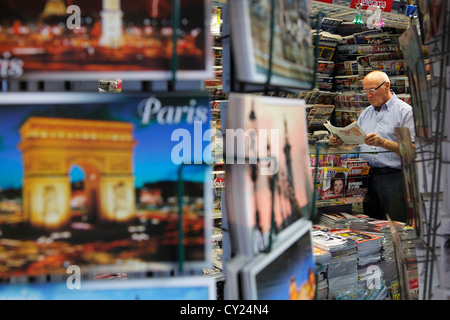 Venditore leggendo un giornale presso il suo stand a Parigi Foto Stock