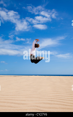 Montare la giovane donna salti di gioia per le dune dall'oceano Foto Stock