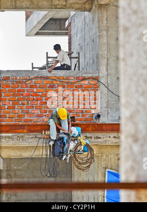 Ingegnere di effettuare le riparazioni di macchinari seduto sul bordo di una trave su di un alto blocco ufficio guardato da un supervisore. Foto Stock