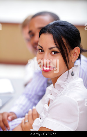 Sorridente business latina donna che guarda la fotocamera con soddisfazione e colleghi di lavoro in ufficio Foto Stock