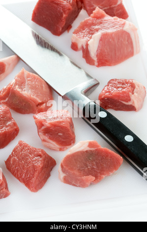 Materie carne di agnello tagliato a dadini con il coltello da cucina e tagliere Foto Stock
