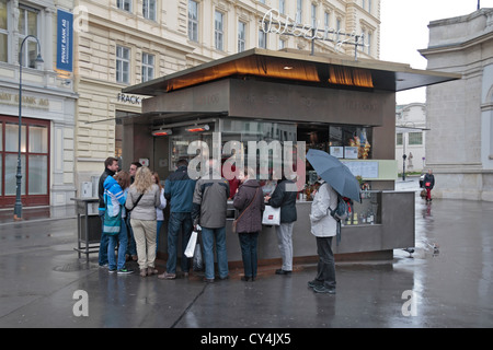 Turisti affamati stanno intorno un wurstel/hot dog fast food chiosco di Vienna in Austria. Foto Stock