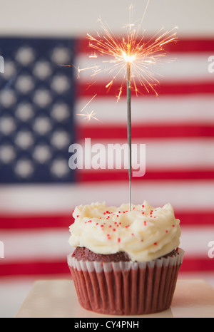 Studio shot di sparkler in cima tortina, bandiera americana in background Foto Stock