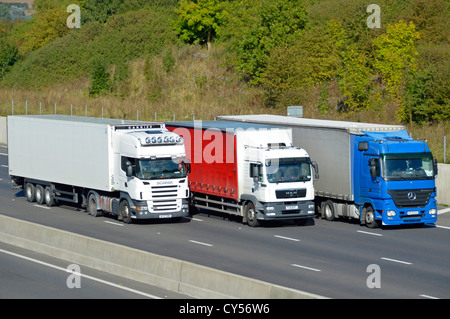 Gruppo di tre viste frontali e laterali sfalsate di colore rosso bianco e i camion blu di trasporto di hgv camion non oversorpasso pubblicitario sopra Autostrada a quattro corsie Inghilterra Regno Unito Foto Stock