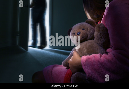 Vista posteriore se un bambino in una stanza buia tenendo un orsacchiotto di peluche, un uomo ha appena lasciato la camera. Foto Stock