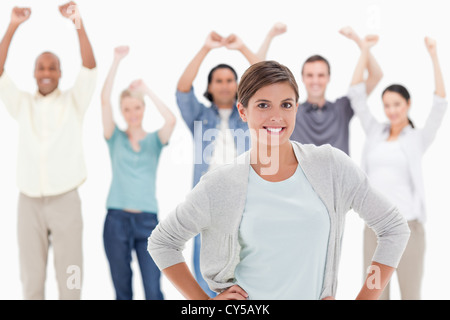 Donna con le mani sui fianchi con persone dietro alzando le braccia Foto Stock