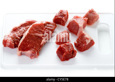 Raw gamba Di agnello bistecche e agnello tagliato a dadini su un tagliere su bianco Foto Stock
