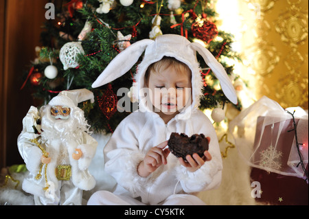 Il nodo albero di Natale si siede un ragazzo vestito come un coniglio bianco Foto Stock