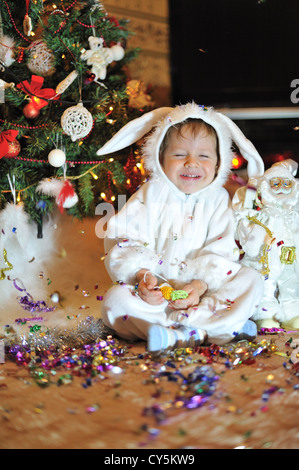 Il nodo albero di Natale si siede un ragazzo vestito come un coniglio bianco Foto Stock