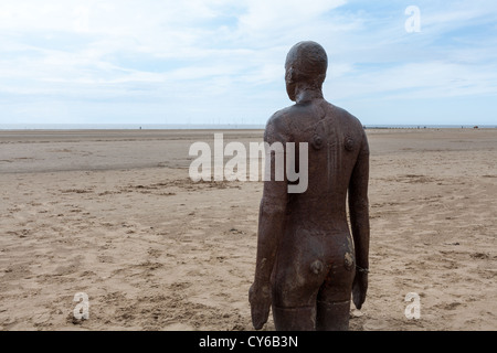 Una delle figure in ghisa da un altro luogo, un pezzo di scultura moderna di Antony Gormley sulla spiaggia di Crosby. Foto Stock