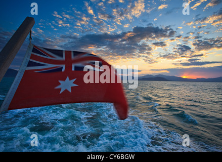 Vista la bandiera australiana e alba dalla barca di lasciare il porto di Cairns per viaggio di tuffo nella Great Barrier Reef Marine Park Foto Stock