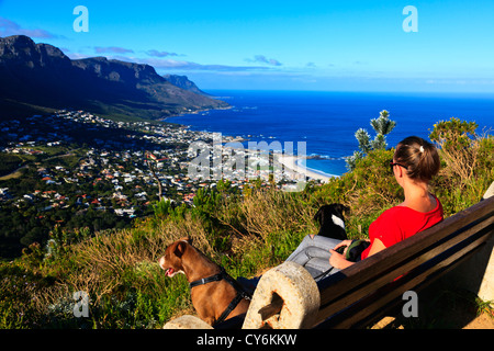 Un giovane turista femminile si siede su un banco che si affaccia Camps Bay vicino a Città del Capo in Sud Africa. Foto Stock