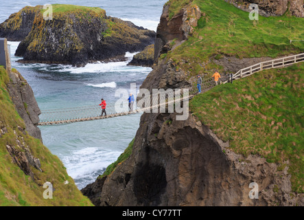 La gente che camminava sul Carrick-a-Rede ponte di corde da Carrick isola alla terraferma nella contea di Antrim, Irlanda del Nord, Regno Unito Foto Stock