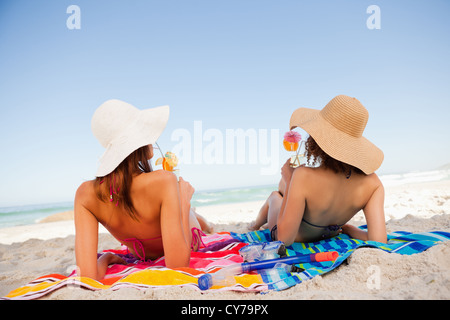 Vista posteriore di belle donne a prendere il sole sorseggiando un cocktail sulla spiaggia Foto Stock