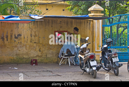 Un uomo di ottenere un taglio di capelli e la barba sul lato strada da un venditore ambulante in Hai Phong Vietnam Foto Stock