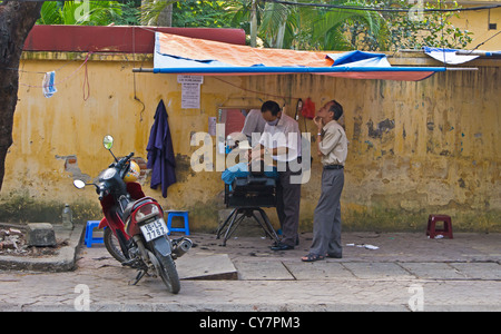 Un uomo di ottenere un taglio di capelli e la barba sul lato strada da un venditore ambulante in Hai Phong Vietnam Foto Stock