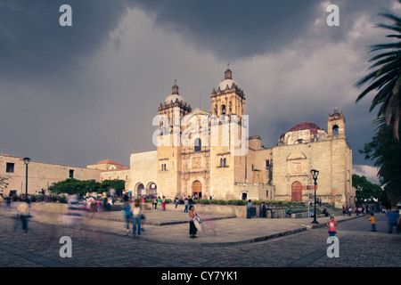 Persone mull intorno alla chiesa di Santo Domingo come si avvicina un temporale in Oaxaca, Messico. Foto Stock