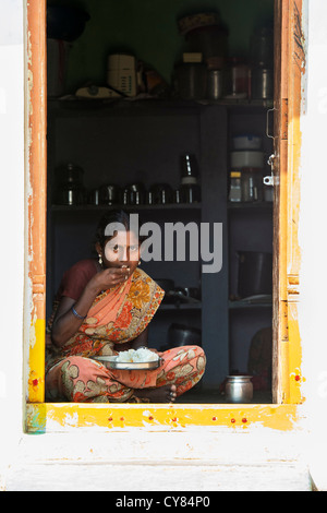 Giovane donna indiana seduto in casa sua porta a mangiare riso. Andhra Pradesh, India Foto Stock