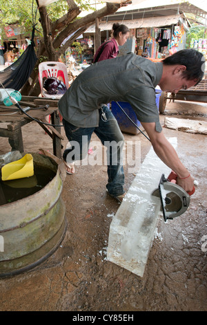 Un commerciante di ghiaccio utilizza una sega circolare per dividere un grosso blocco di ghiaccio in O'Ambel mercato, Sisophon, Cambogia Foto Stock