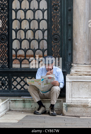 Anziano gentiluomo seduto sui gradini della Basilica di San Marco a Venezia, leggendo un giornale e fumare una tubazione. Foto Stock