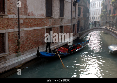 Una gondola prende i turisti per un giro lungo uno dei canali più piccoli a Venezia, Italia Foto Stock