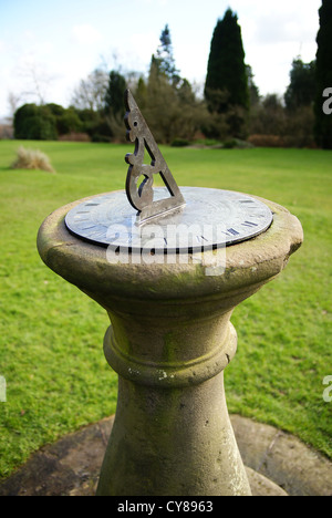 Un orologio solare su uno zoccolo in pietra in un ambiente da giardino Foto Stock