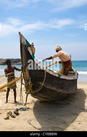 Ritratto verticale di pescatori reti da traino su una barca sulla spiaggia di Kovalam, Kerala. Foto Stock