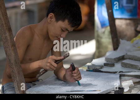 Un giovane ragazzo nel cimitero Calamba,Cebu, Filippine scolpisce una lapide durante tutti i Santi e la Commemorazione di Tutti i Fedeli Defunti celebrazioni. Foto Stock