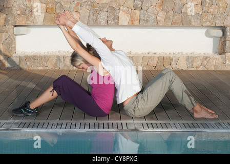 Coppia giovane seduto di schiena a bordo piscina stretching Foto Stock