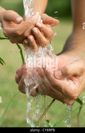 A coppa le mani sotto acqua corrente all'aperto Foto Stock