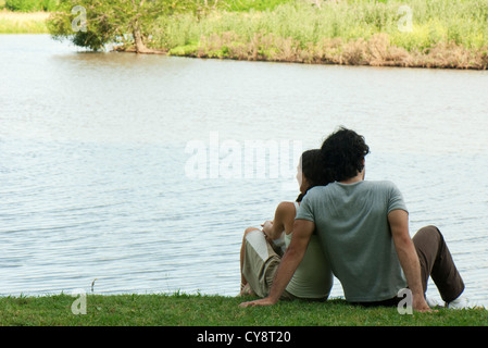 Giovane seduti insieme dal lago, vista posteriore Foto Stock