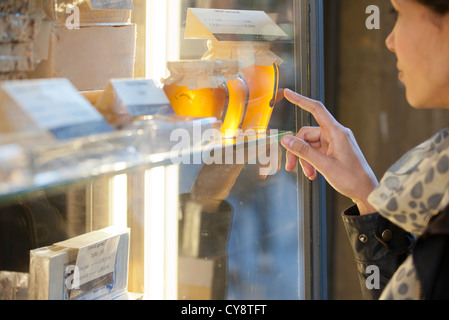 Donna che guarda a vasetti di miele in vetrina Foto Stock