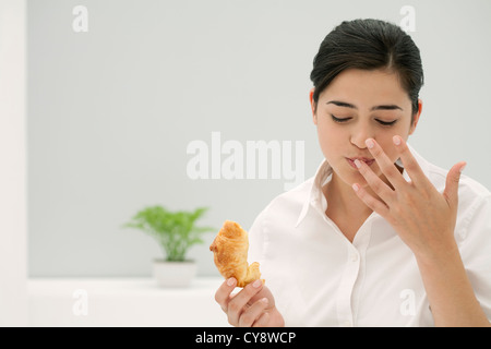 Giovane donna leccare il dito mentre mangiare croissant Foto Stock