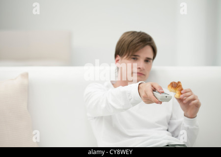 Giovane uomo guardando la TV, cambiare canale con il telecomando Foto Stock