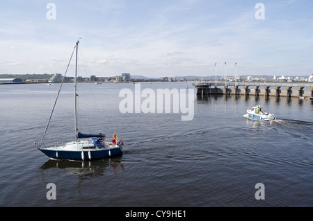 Una barca a vela e una piccola barca da pesca appena lasciando la baia di Cardiff Barrage Galles. Vista dello sbarramento e dello skyline della città Foto Stock