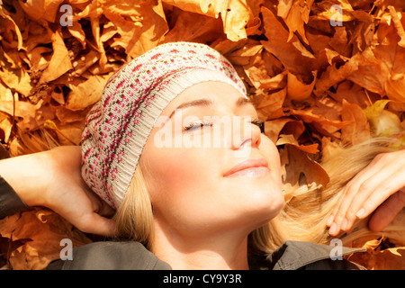 Foto di carina ragazza bionda sognare sul suolo coperto di colore arancione foglie autunnali in giardino, bella donna rilassata Foto Stock