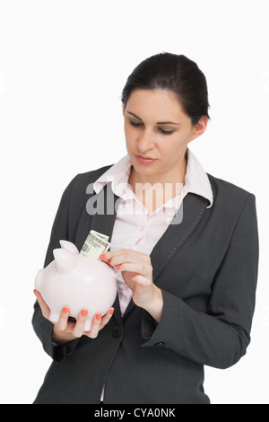 Bruna in tuta di dollari mettendo in un piggy-bank Foto Stock