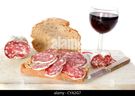 Fette di salsiccia francese sul pane con coltello, vino e pane di fronte a uno sfondo bianco Foto Stock