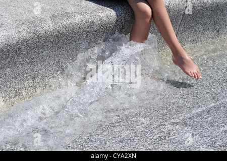 Le gambe di una giovane donna che si sta raffreddando in Diana Memorial Fountain su un giorno d'estate a Londra Foto Stock