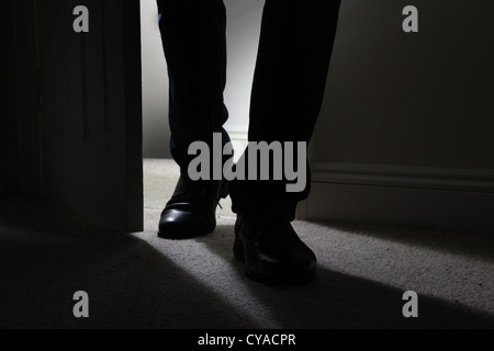 Maschio nero da indossare scarpe di entrare in una stanza buia, back lit. Close up sinister male Foto Stock