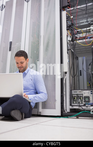 Uomo al lavoro con il suo computer portatile sul pavimento accanto al server Foto Stock