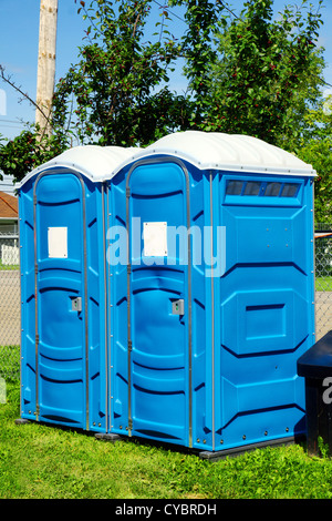 Due WC portatili o loo in plastica blu al parco per un evento pubblico o di concerto, con segno bianco sulla porta pronto per il testo.